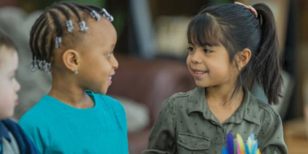 Two little girls smiling at one another.