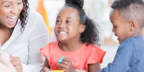 Teacher playing and smiling with two of her preschoolers.