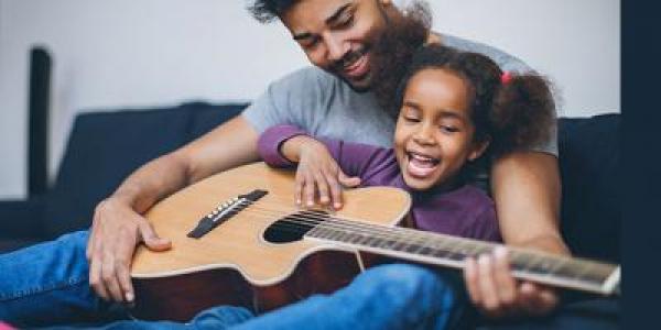 Father and daughter playing guitar on couch