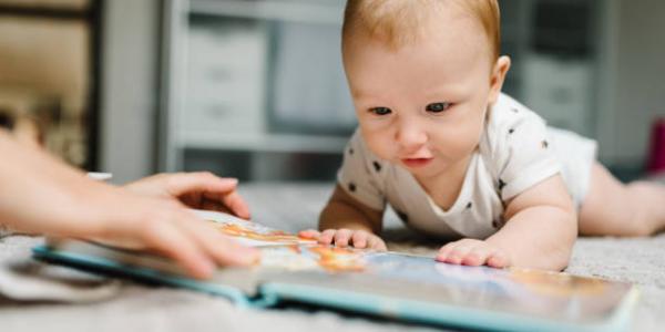 A baby on the floor with a book.