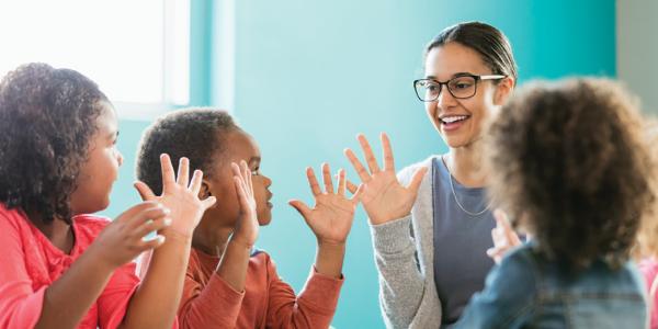 Teacher and three preschool students with hands up