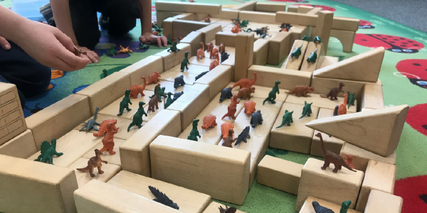 Children play with blocks and dinosaur figurines.