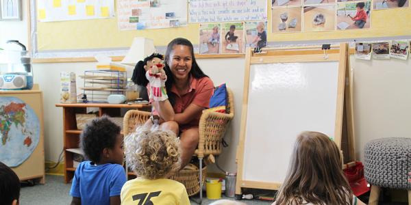 feature teacher cecilia fowler with children playing with a puppet