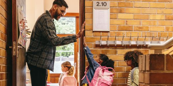 A male teacher high fiving a student on the way into the classroom