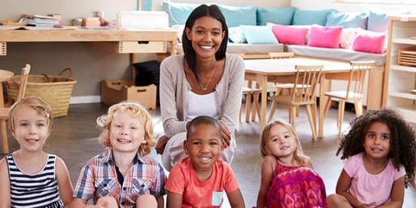 A female teacher poses for a picture with 6 young children.