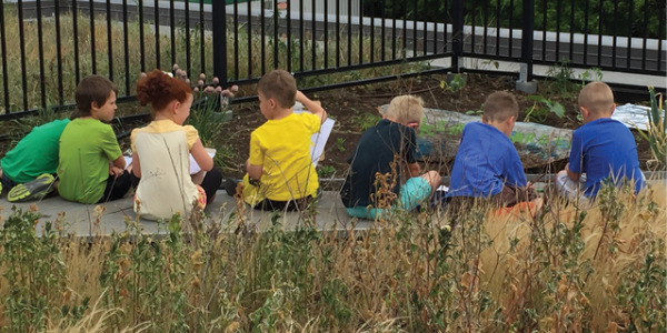 Row of children sitting outside near a garden