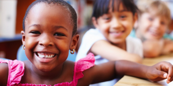 Three children smile while sitting at a table.