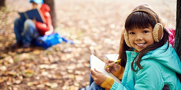 A young girl draws and takes notes in a forest