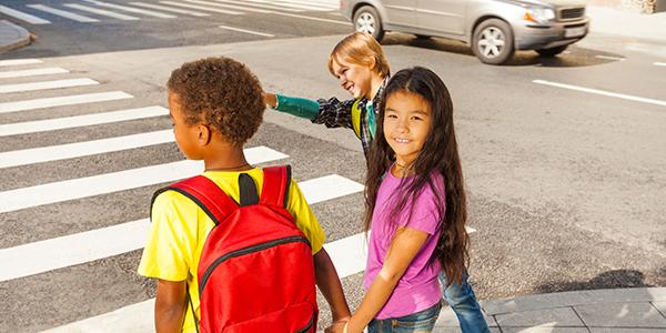 Three children of different races and ethnicities walk to school together.