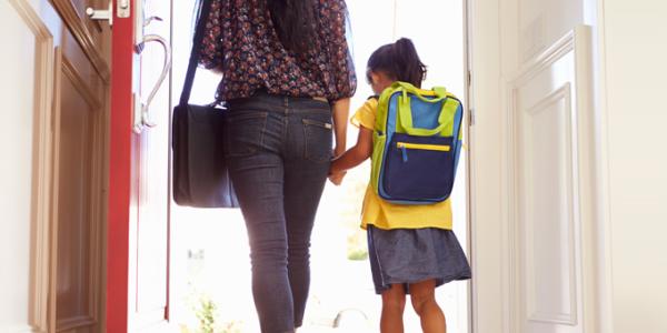 Parent holding daughters hand and walking through the door.