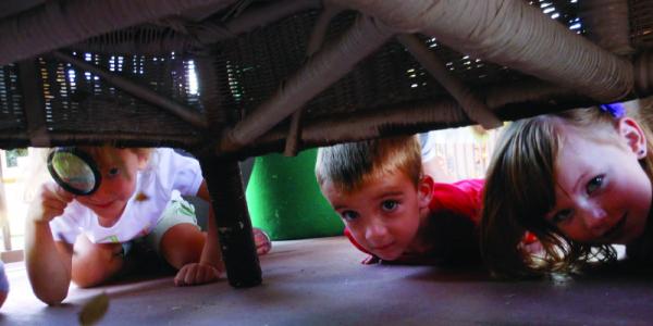 Children searching with magnifying glass under furniture. 