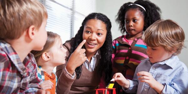 Teacher and preschool age students sitting at table with materials