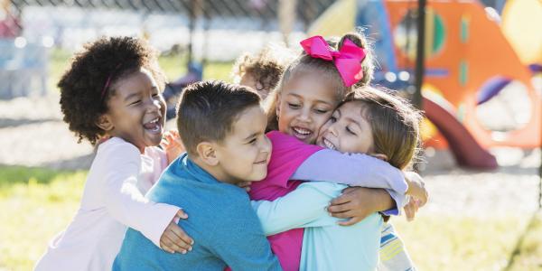 Group of diverse young children hugging on the playground