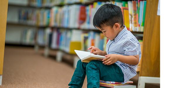 Preschool boy reading a book in the library