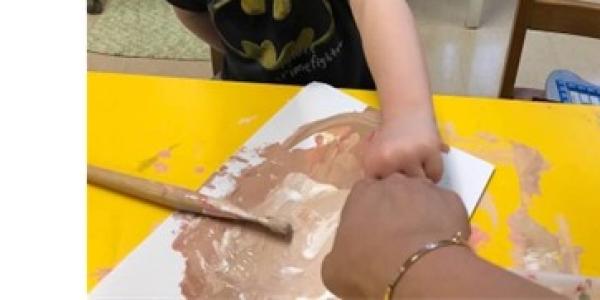 A child and teacher mixing brown paint together to match skin tones.