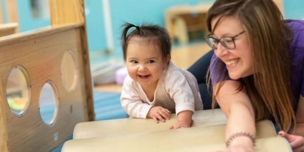 A teacher helping a toddler learn to crawl