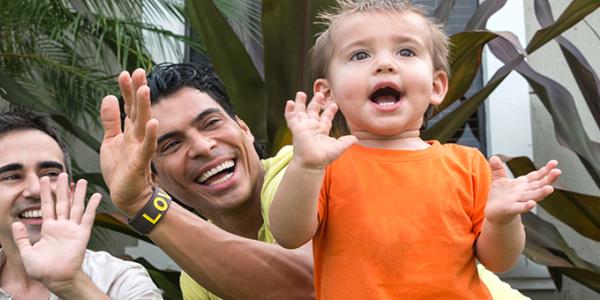 Two male parents play outdoors with their child.