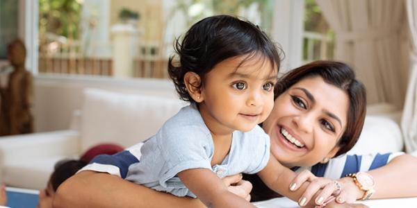 Toddler climbing on table with mother holding her.