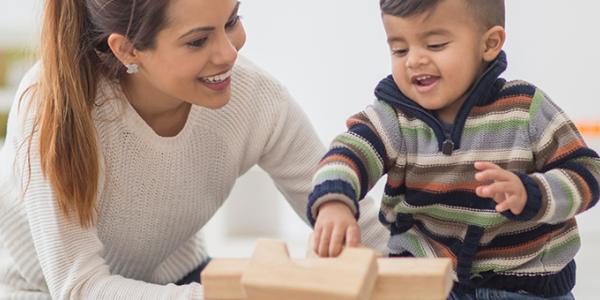 An adult woman helps a young male child with blocks. 