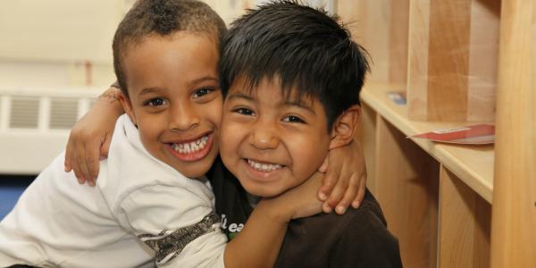 Two young boys of color embrace and small into the camera.