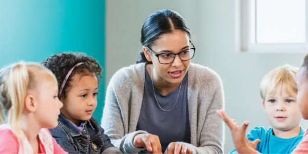 A teacher talking with a group of young children.