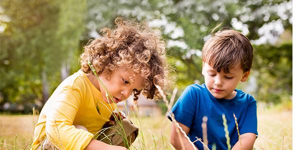 Young children exploring in the grass outside.