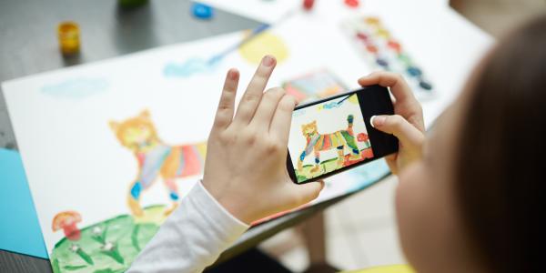 A child taking a picture of their artwork with a smartphone.
