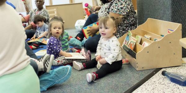 Toddlers playing in a classroom on the floor, sitting with three teachers