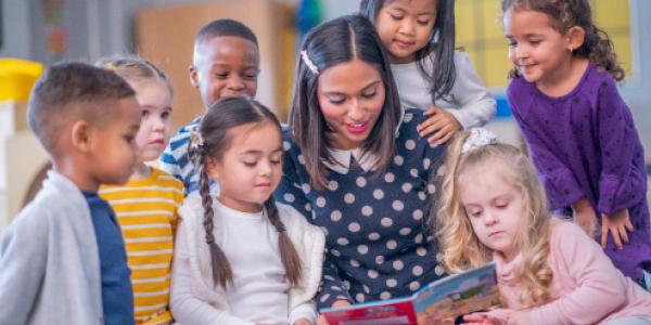 teacher with children gathered around a book