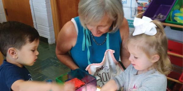 Feature Teacher Bonnie Sears works with two children at the light table.