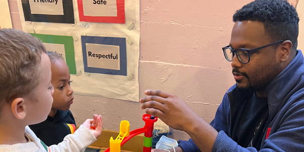 A teacher playing with plastic blocks with children.