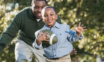 Father and son running and playing with a football outdoors