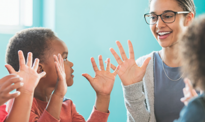 Teacher and three preschool students with hands in air