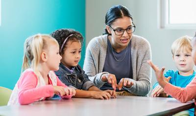 Preschool teacher guides students at table