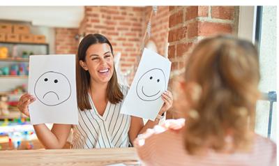 A parent shows a child a picture of a happy and a sad face.