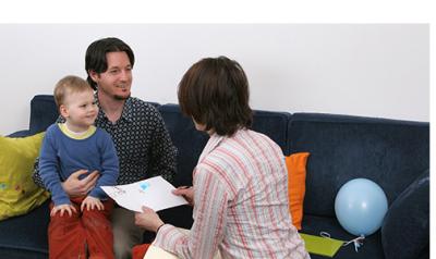 a parent holding a child with a teacher showing them something