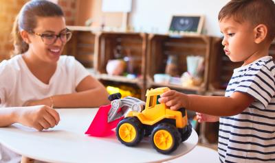 A teacher interacting with a child playing with a truck toy.