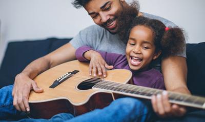 Father and daughter playing guitar on couch