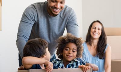 Two young boys playing in a box with mother and father smiling behind them