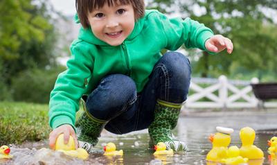 Young child playing with rubber duckies in a puddle outside