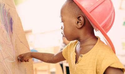 Young boy drawing on a canvas wearing a red hat