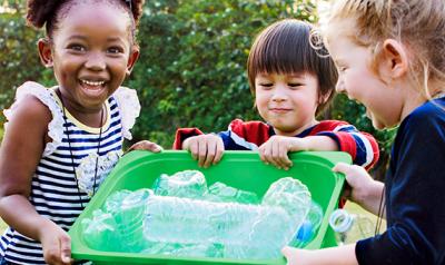 Diverse preschoolers holding a recycling bin with plastic bottles