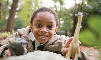 Boy playing outdoors with toy dinosaur