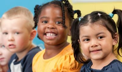 Young children in a line smile for a photograph. 