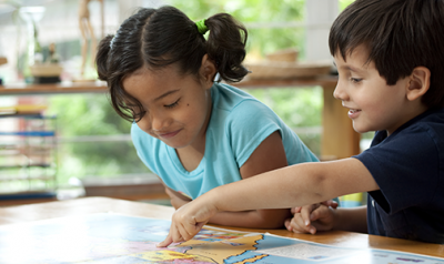 A young boy and girl pointing at a map on a desk in the classroom