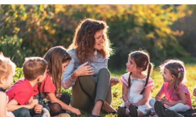 a teacher surrounded by young children outside