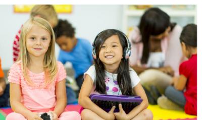 two young children happily sitting side by side. one of the children is wearing headphones