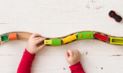 A child's hands can be seen guiding a toy train down a wooden track