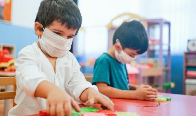 Two children playing in a classroom wearing protective masks.