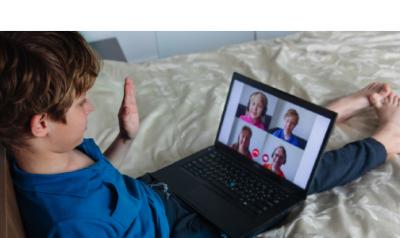 a young boy waving at other children on a video call on the computer 